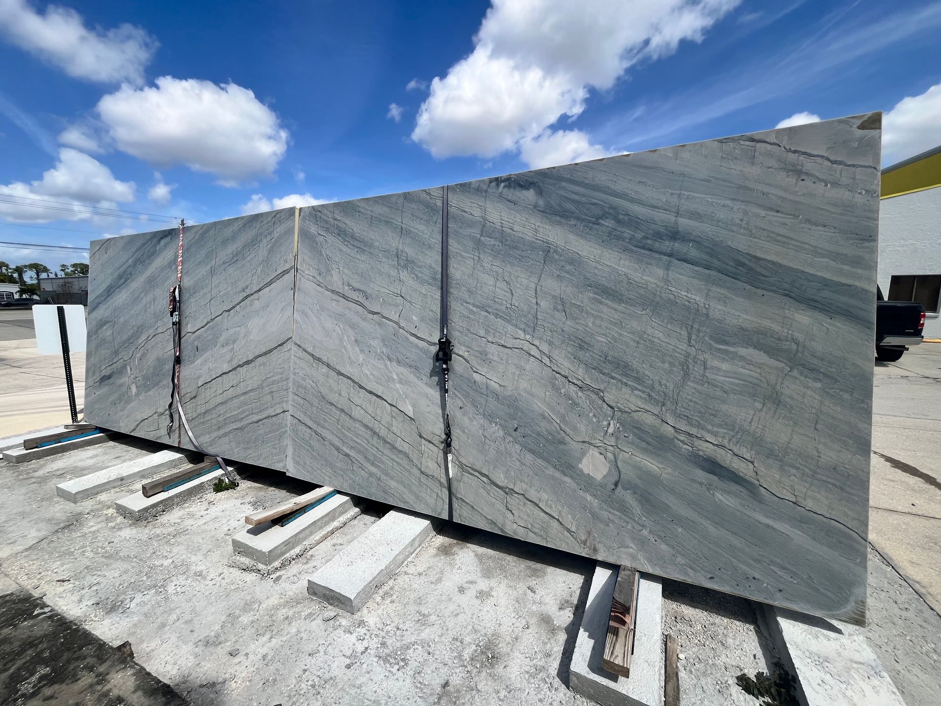 A large, grey stone slab with diagonal chevron veining stands outdoors under a blue, cloudy sky.