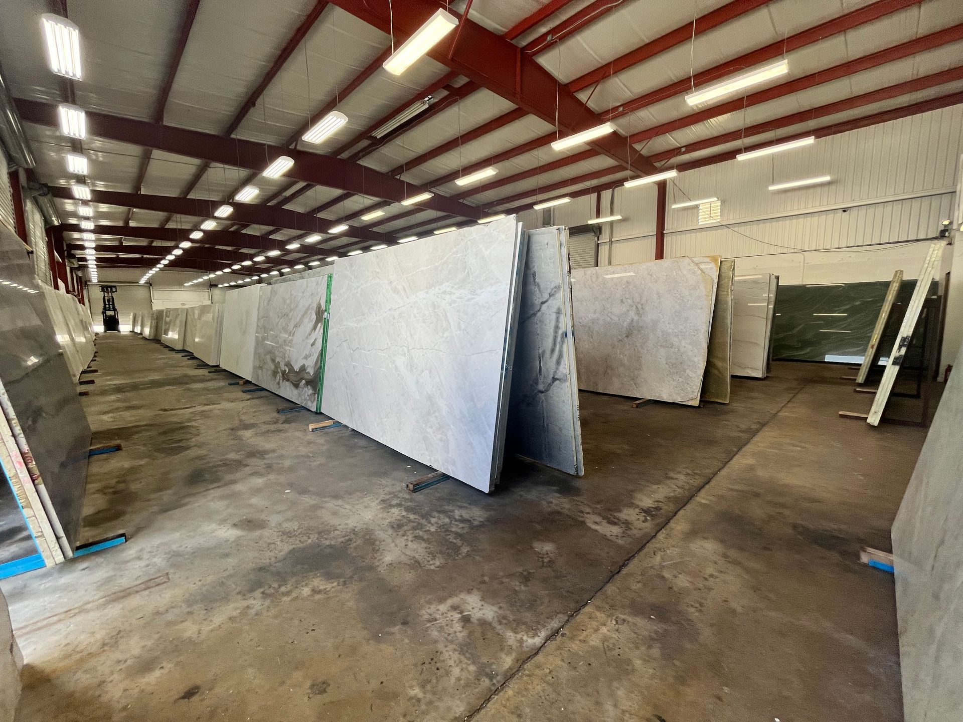 A warehouse interior showing rows of upright large stone slabs with light grey and white veining on a concrete floor.