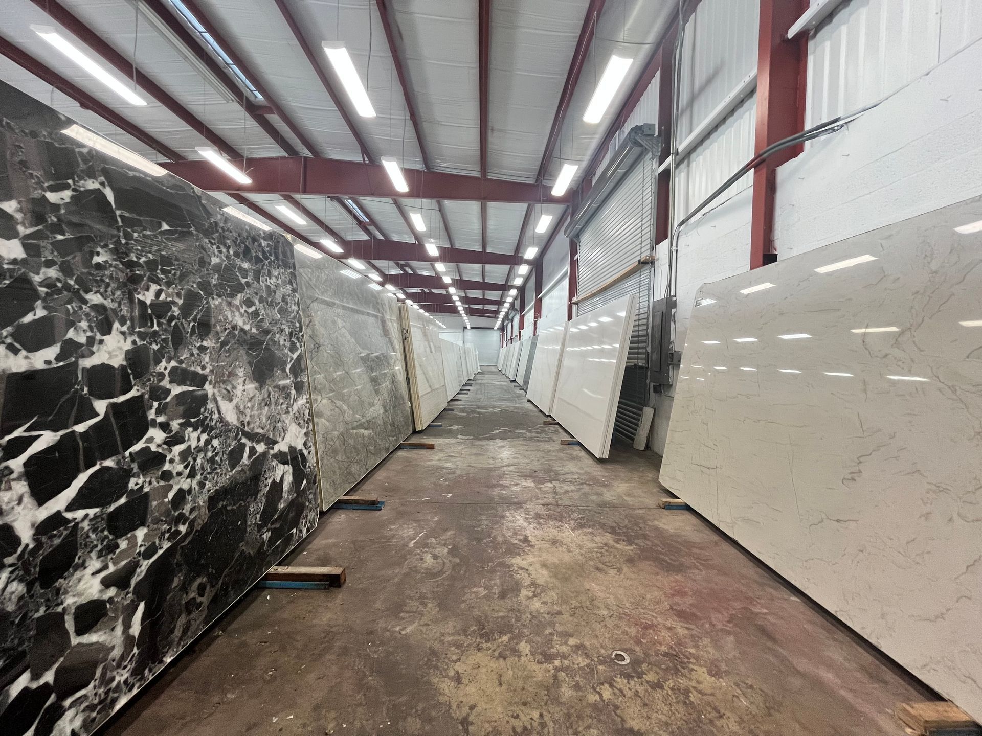 Large stone slabs for countertops lined up on both sides of a warehouse aisle under bright overhead lighting.