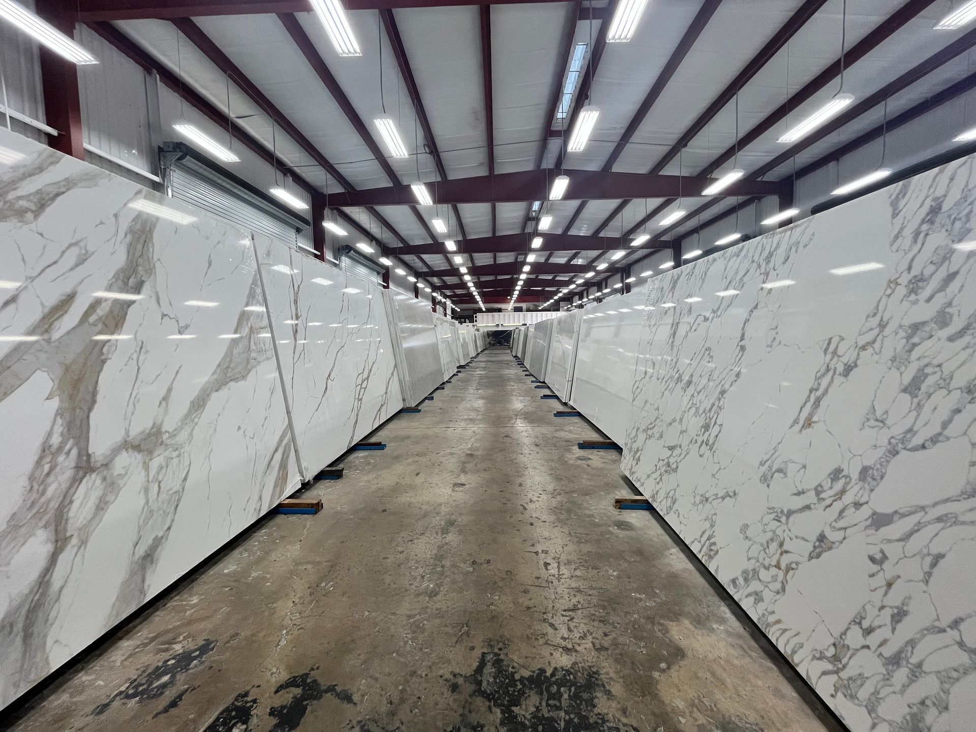 Large slabs of white marble with gray veining stand upright in parallel rows inside a warehouse with overhead lighting.