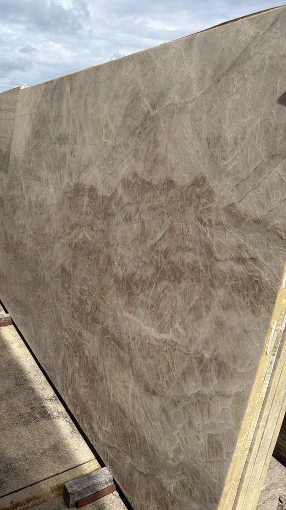 Large gray textured panel standing outdoors beside a sidewalk under a partly cloudy sky