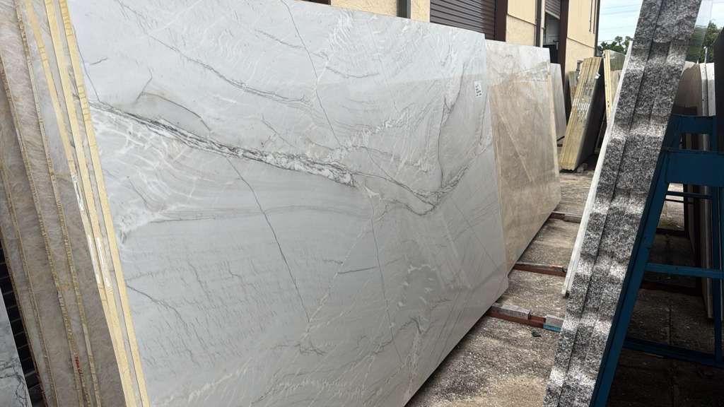 Large white marble slab with gray veining leaning in an outdoor stone yard