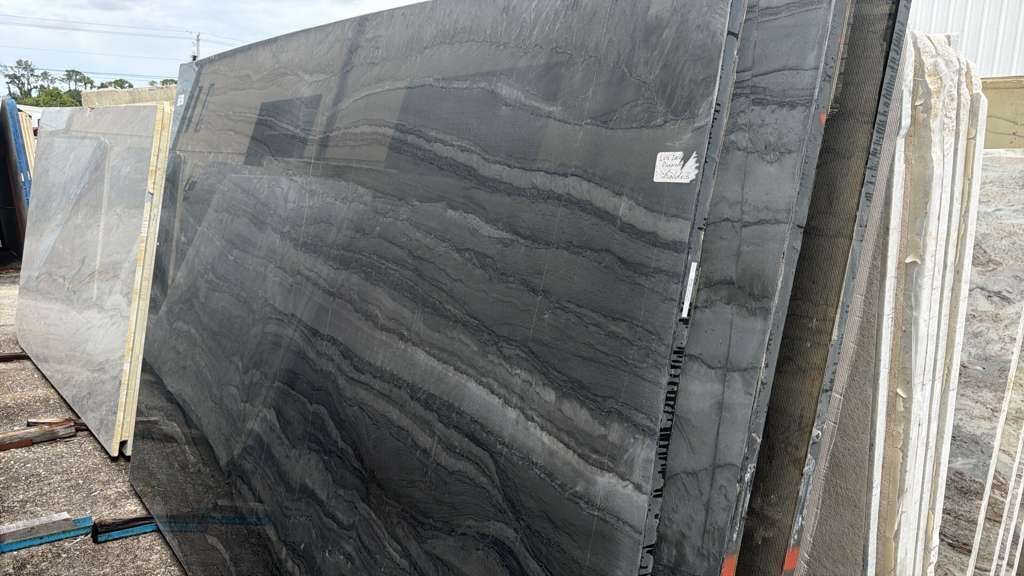 Stacked large dark stone slabs outdoors in a storage yard