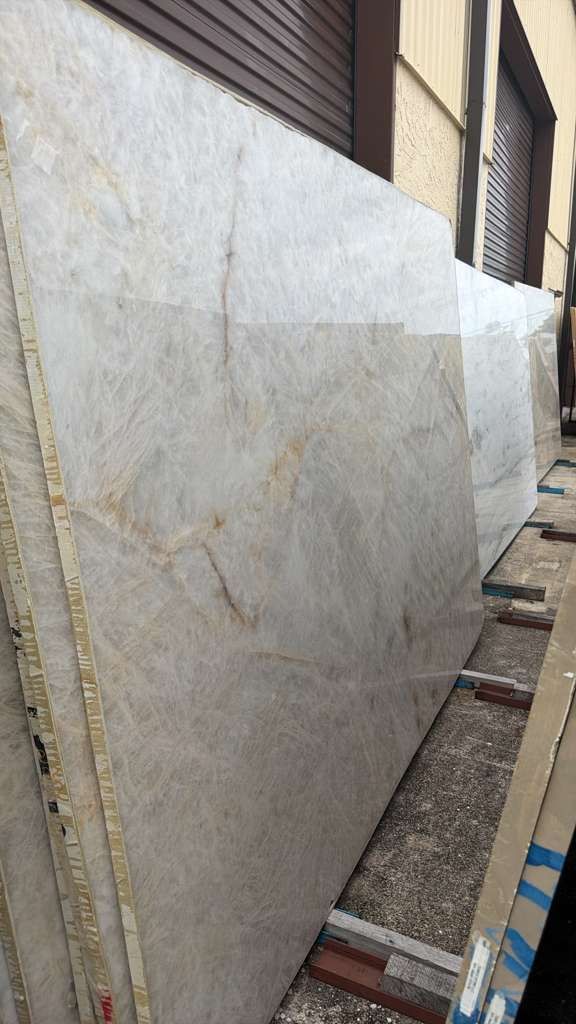 Large light-gray marble slab leaning against a wall in a narrow outdoor passage.