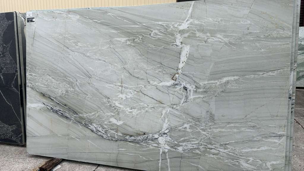 Gray marble slab with white veining and a central crack, displayed vertically outdoors
