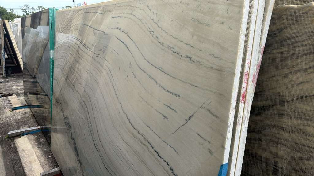 Large beige marble slabs stacked upright in a stone yard, with gray veining visible