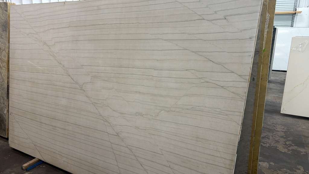 Stacked white marble slabs in a warehouse, with one large slab leaning in the foreground.