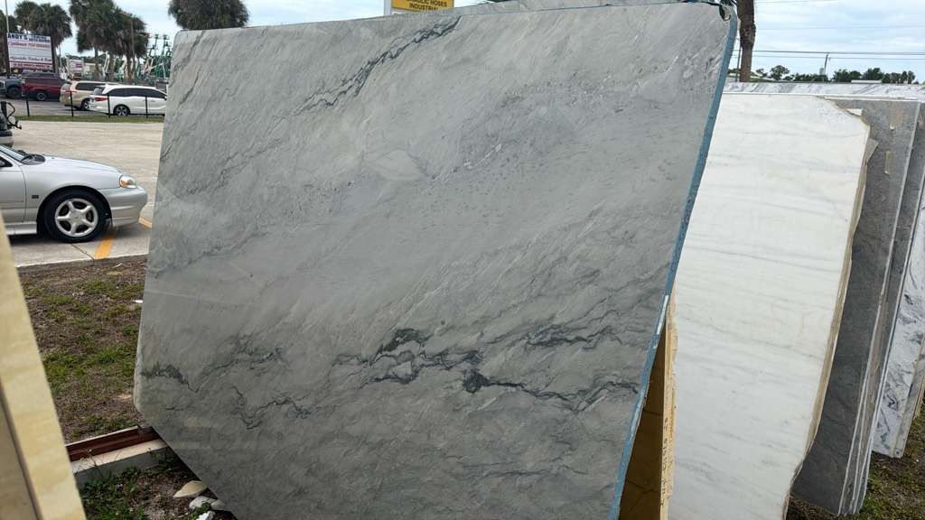 Large gray stone slab displayed outdoors beside a white stone slab at a roadside lot