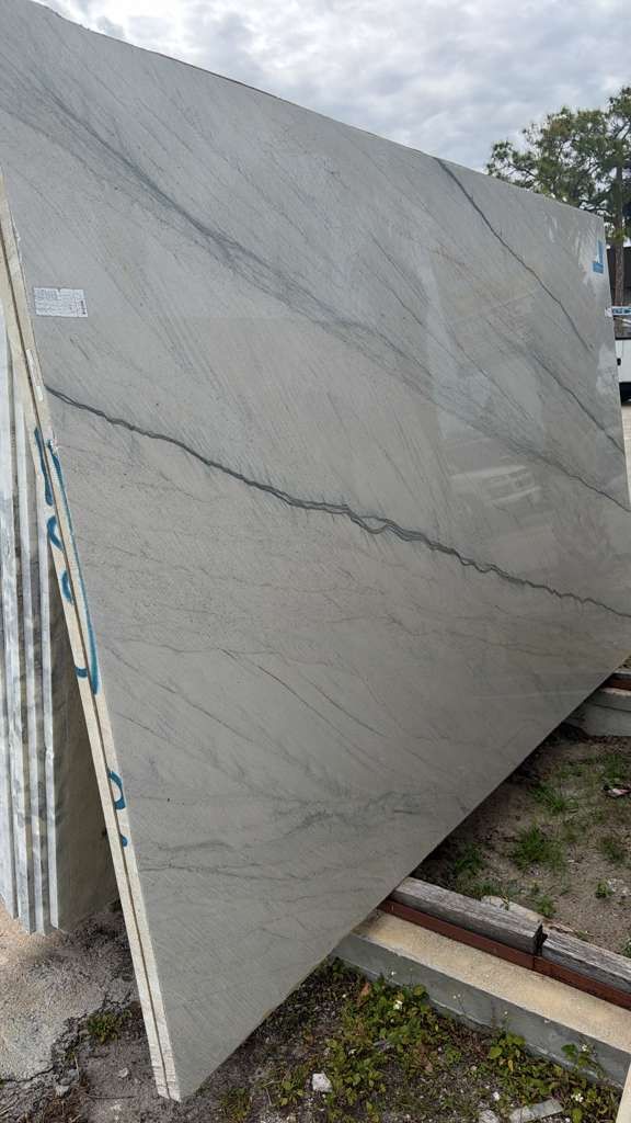Large gray stone slab leaning outdoors, with dark veining and rough edges.