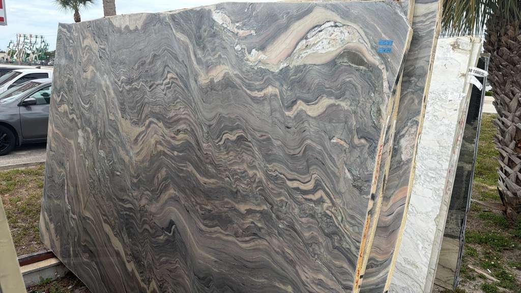 Large polished gray marble slab with wavy veining displayed outdoors in a stone yard