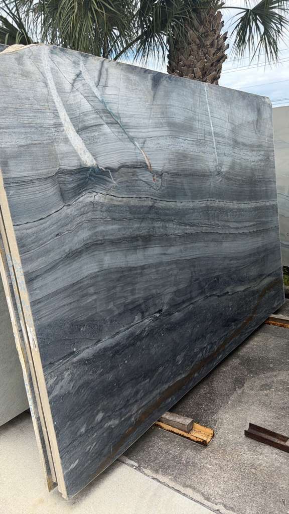 Large gray-and-black veined stone slab leaning outdoors on a wooden support