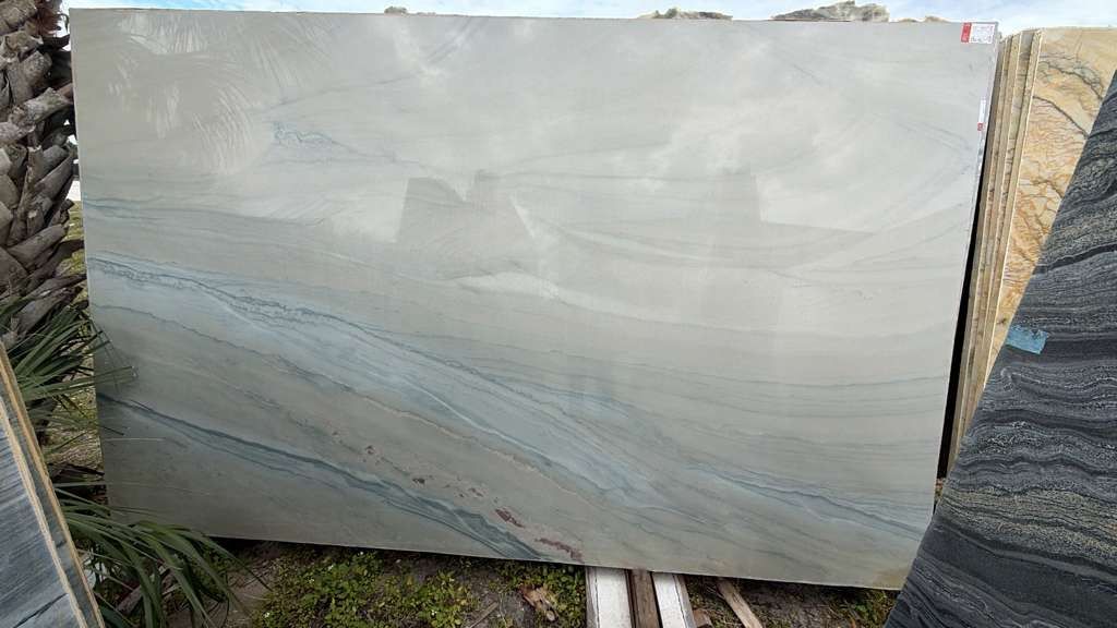 Large light gray stone slab with subtle blue-gray veining leaning outdoors against other slabs