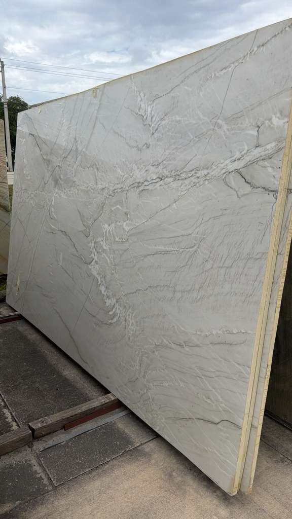 Large white stone slab standing upright outdoors on pavement, with gray veining and wooden edge supports