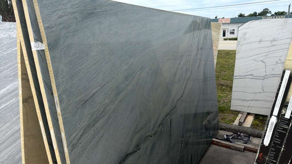 Large gray stone slab leaning outdoors beside a white marble slab on a gravel lot.