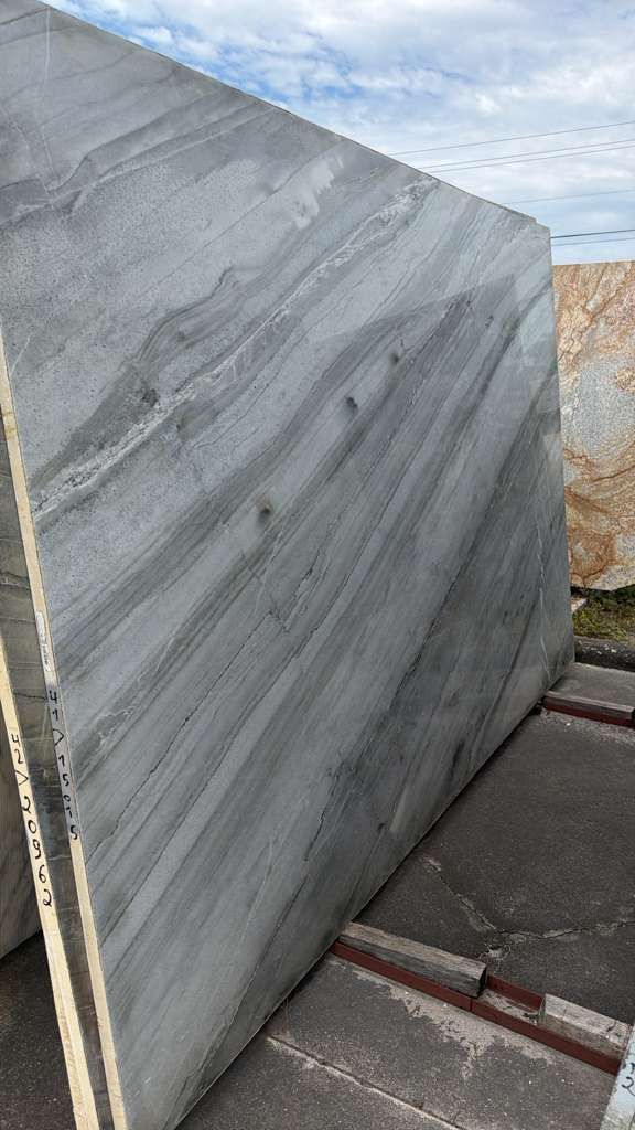 Large gray marble slab standing outdoors on a platform, with cloudy sky in the background