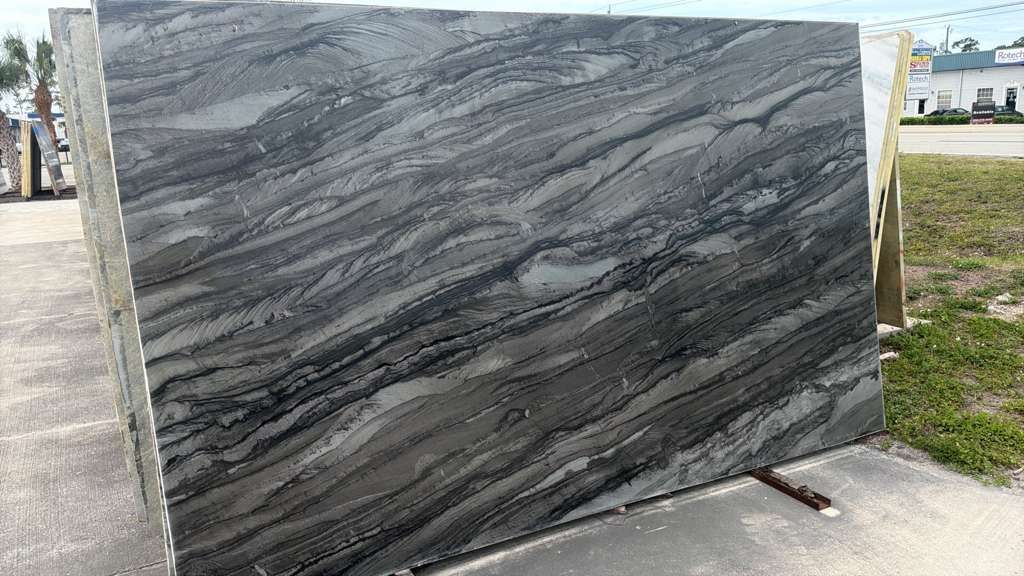 Large polished gray granite slab with black veining displayed outdoors on a sidewalk