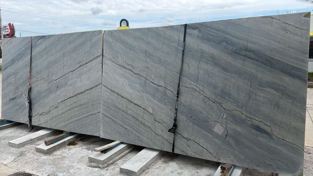 Large gray stone slab with diagonal veining, stacked on wooden pallets outdoors.