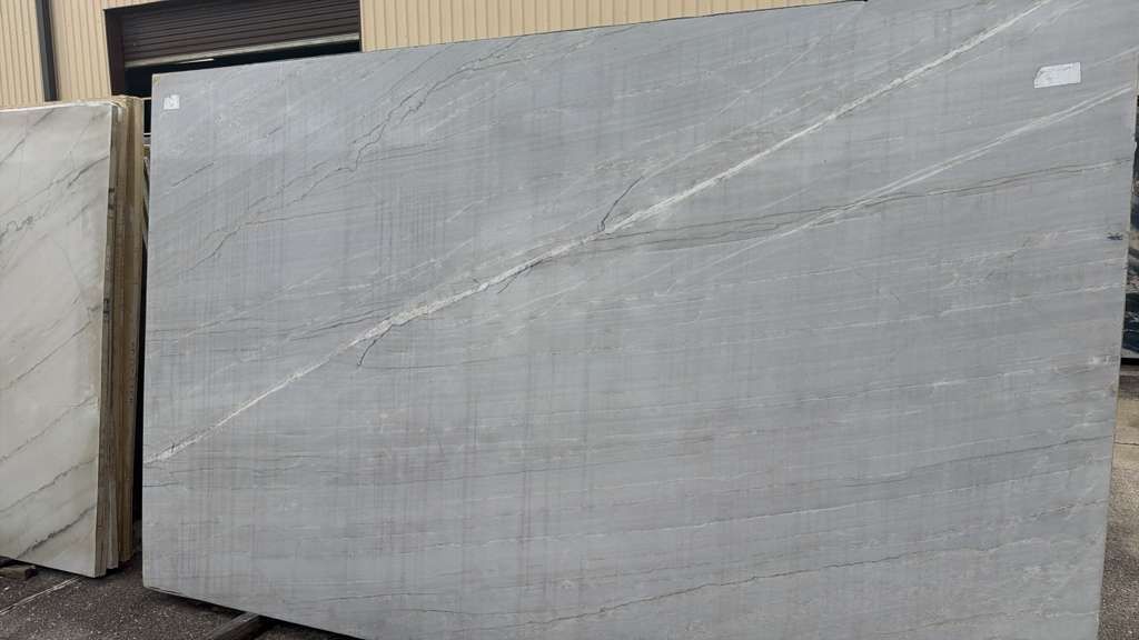Large gray stone slab leaning against a wall in an outdoor industrial area