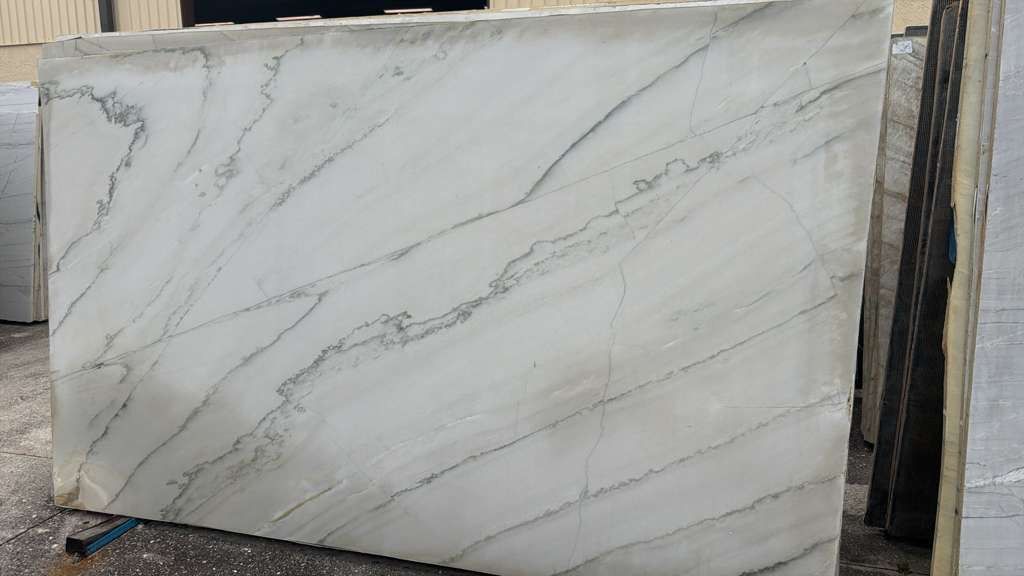 Large white marble slab with gray veining leaning outdoors against a wall.