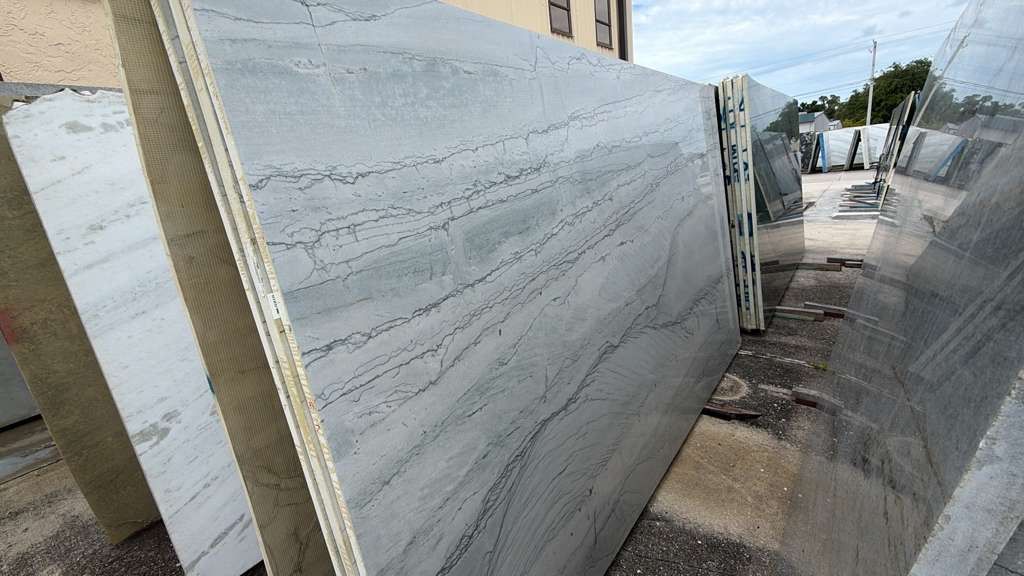 Large white marble slabs stacked outdoors along a narrow industrial yard path
