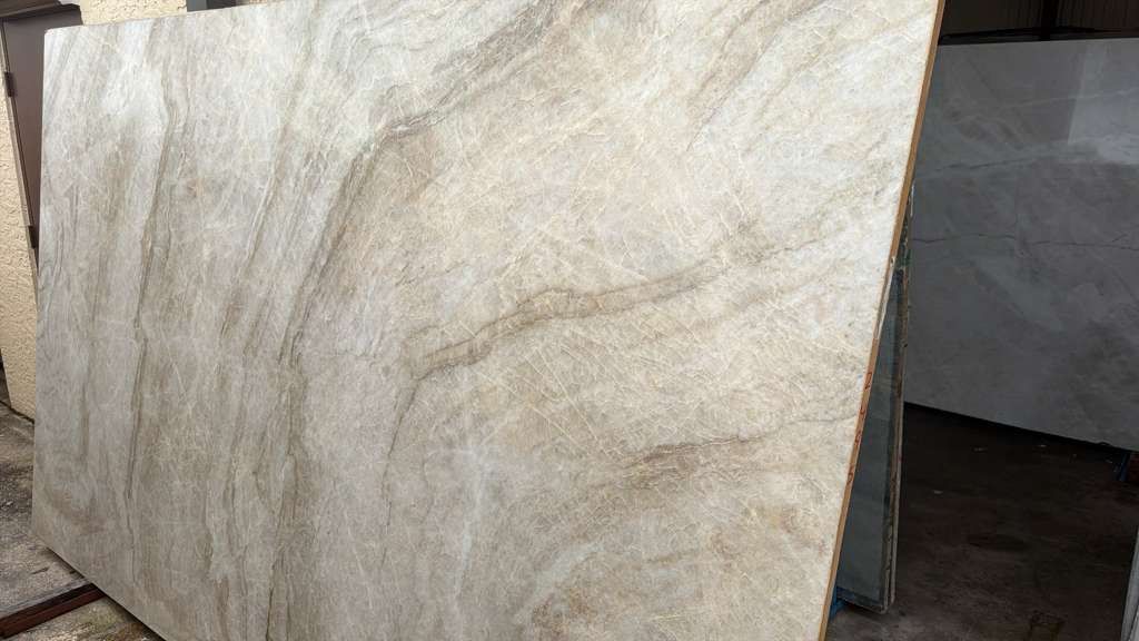 Large beige stone slab with natural veining, leaning outdoors against a dark structure.