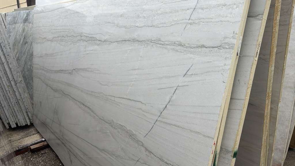 Large white stone slabs with gray veining stacked outdoors in a yard