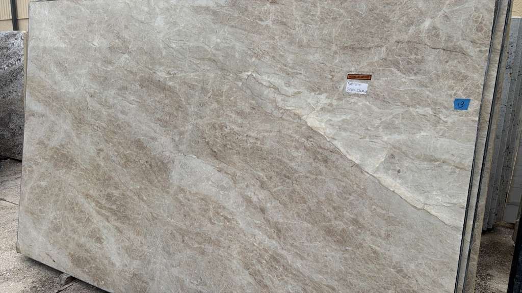 Large beige marble slab with subtle veining, displayed upright in a stone yard