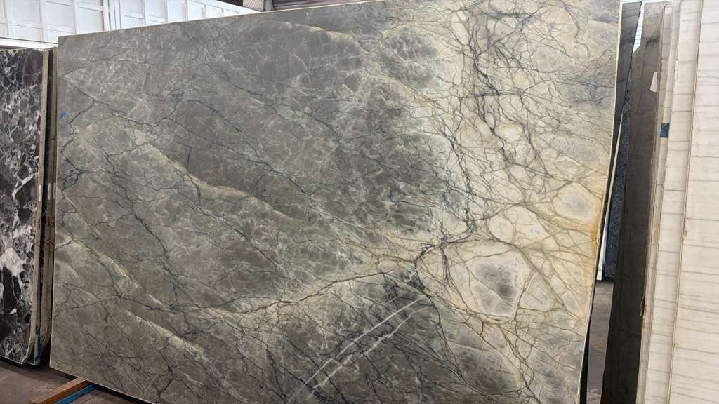Large gray-green marble slab with veined patterns, displayed upright in a stone yard