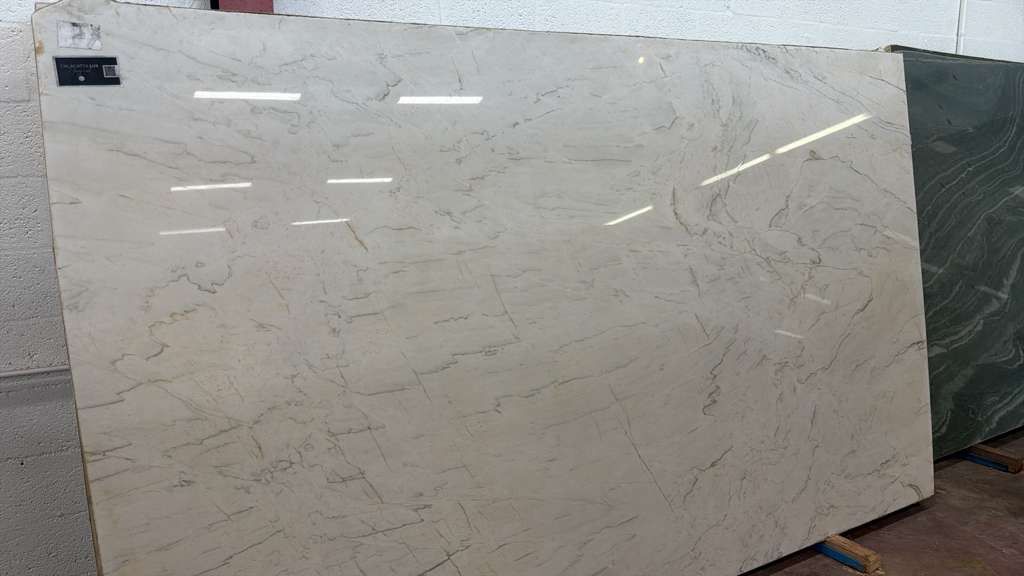 Large white marble slab with light gray veining leaning against a wall in a warehouse-like setting.