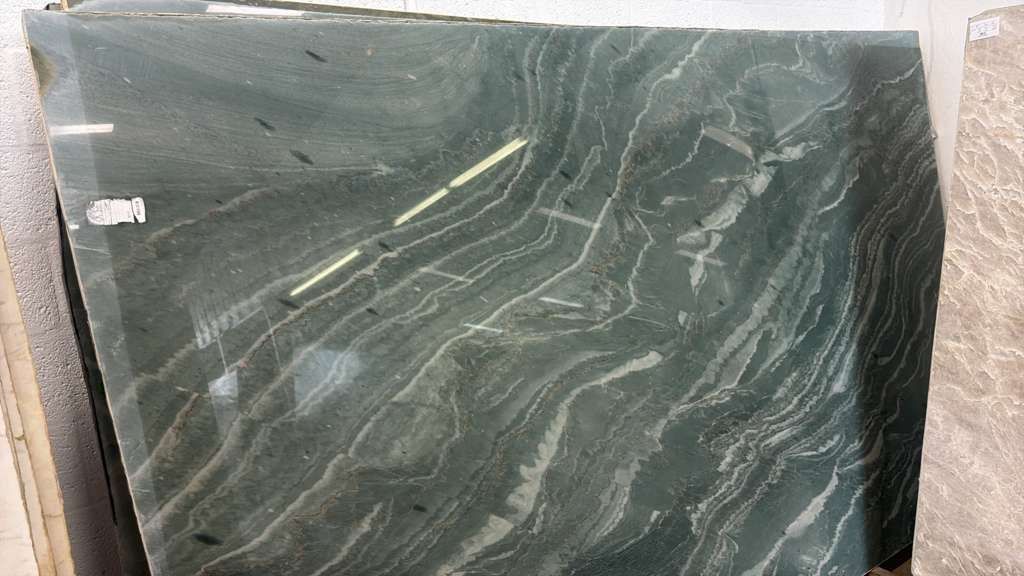 Dark green polished stone slab with white veining, leaning against a wall.