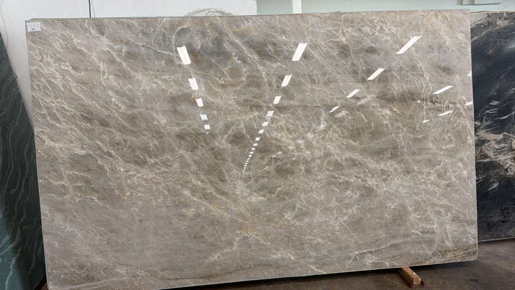Large polished gray stone slab with white veining, leaning upright in a workshop or warehouse.