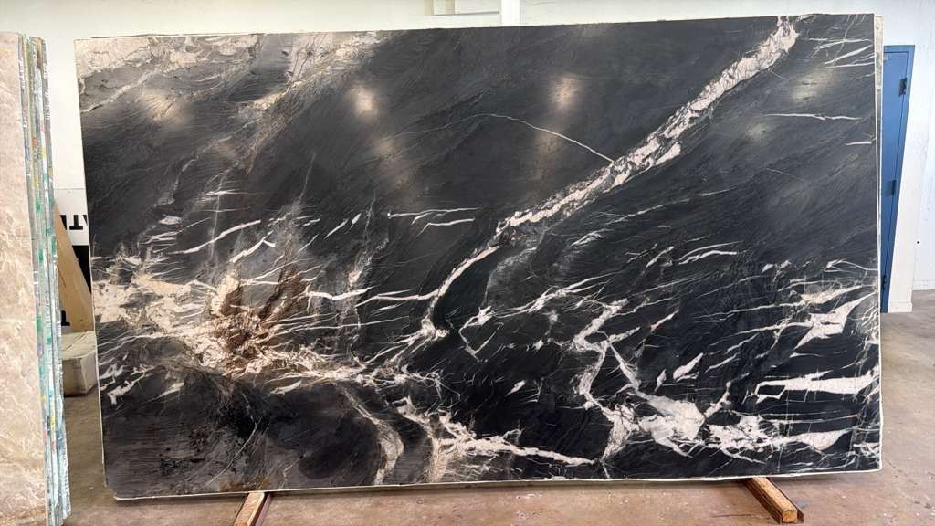 Large black marble slab with white veining on a wooden stand in a workshop or showroom