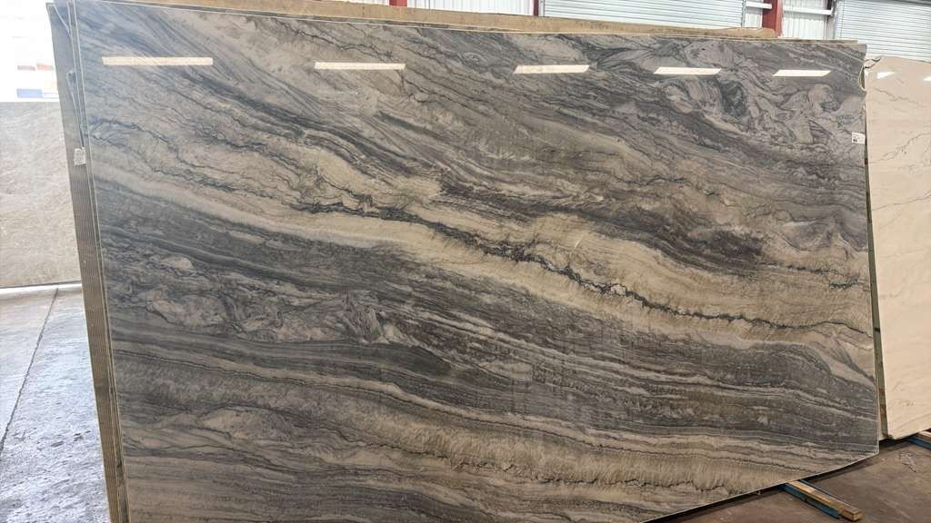 Large polished stone slab with gray and tan wavy veining, standing upright outdoors