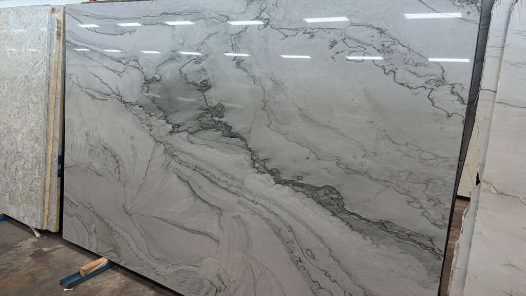 Large polished white-gray marble slab with dark veining displayed upright in a warehouse or showroom.