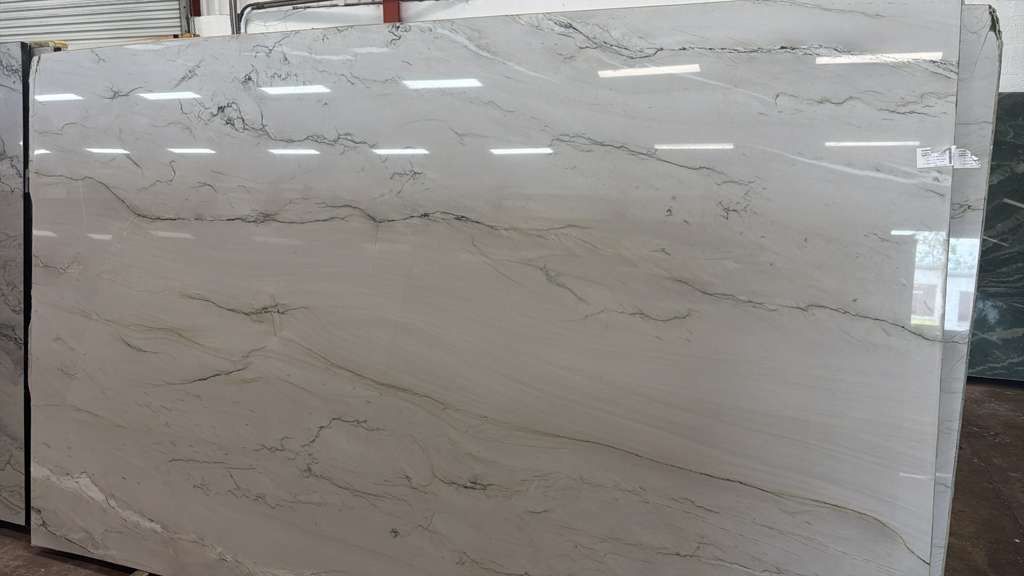 Large beige marble-look stone slab with subtle gray veining, displayed upright indoors on a showroom floor
