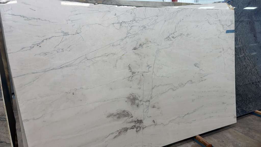 Large white marble slab with gray veining leaning upright in a warehouse or stone yard.