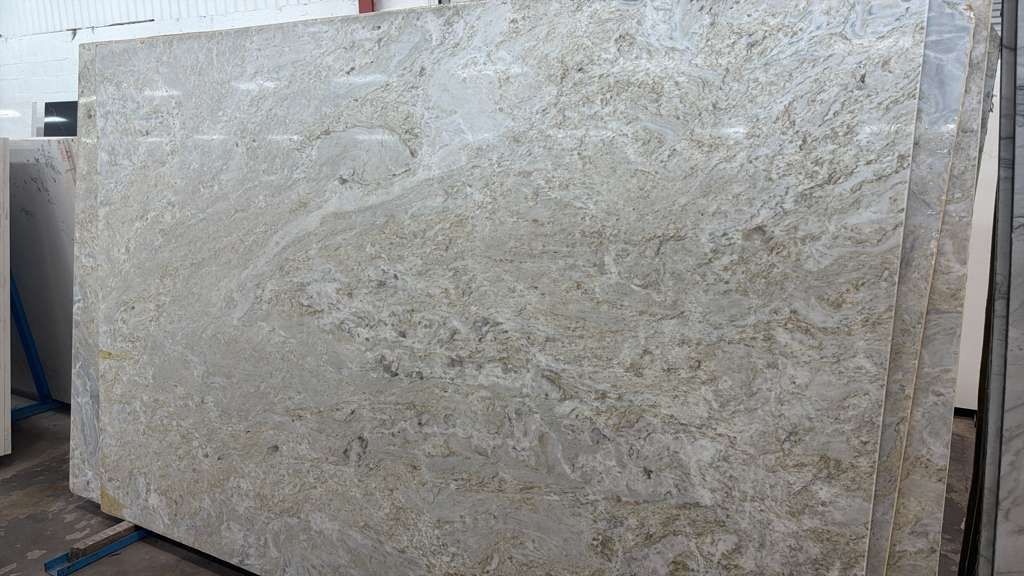 Large beige stone slab with a speckled textured surface, leaning upright in a warehouse or showroom.