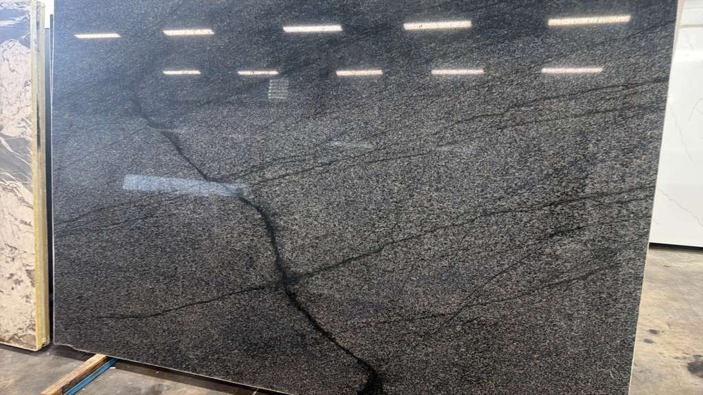 Black polished stone slab with a diagonal crack and reflective lights overhead