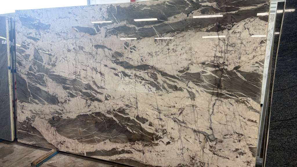 Large beige-and-black marble slab leaning against a wall outdoors