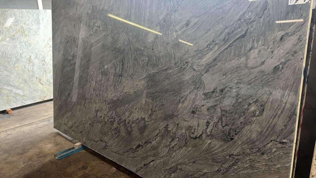Large polished gray marble slab leaning upright in a stone workshop, with another slab visible to the left.