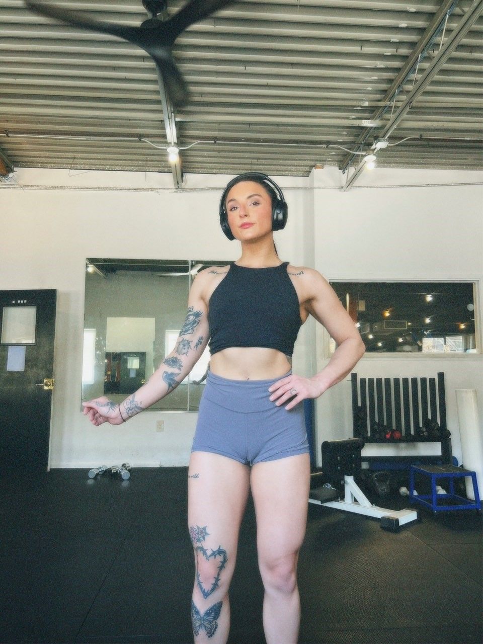 A woman wearing headphones and shorts is standing in a gym