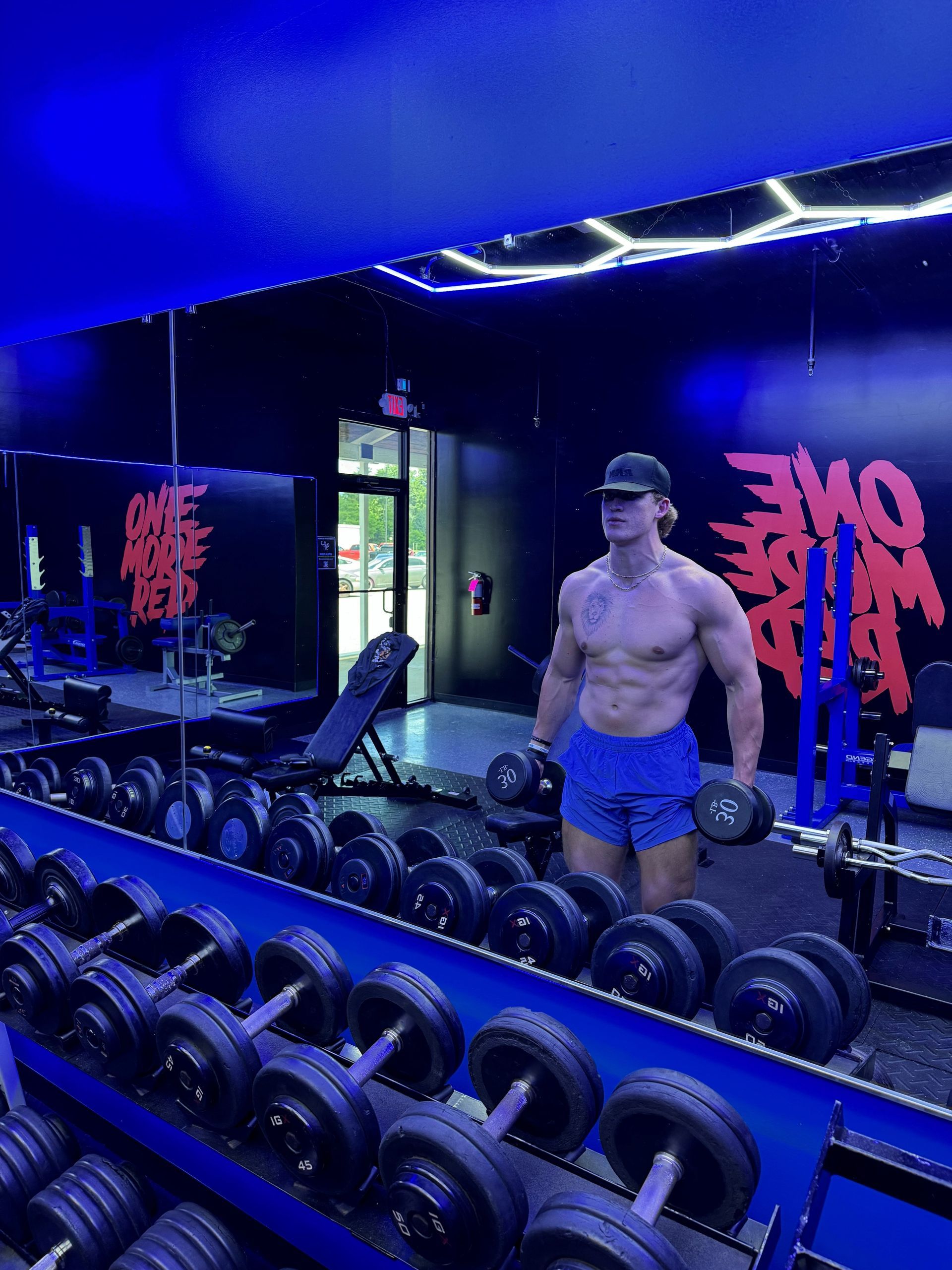 Jack Mulhern is standing in front of a mirror in a gym holding a dumbbell.