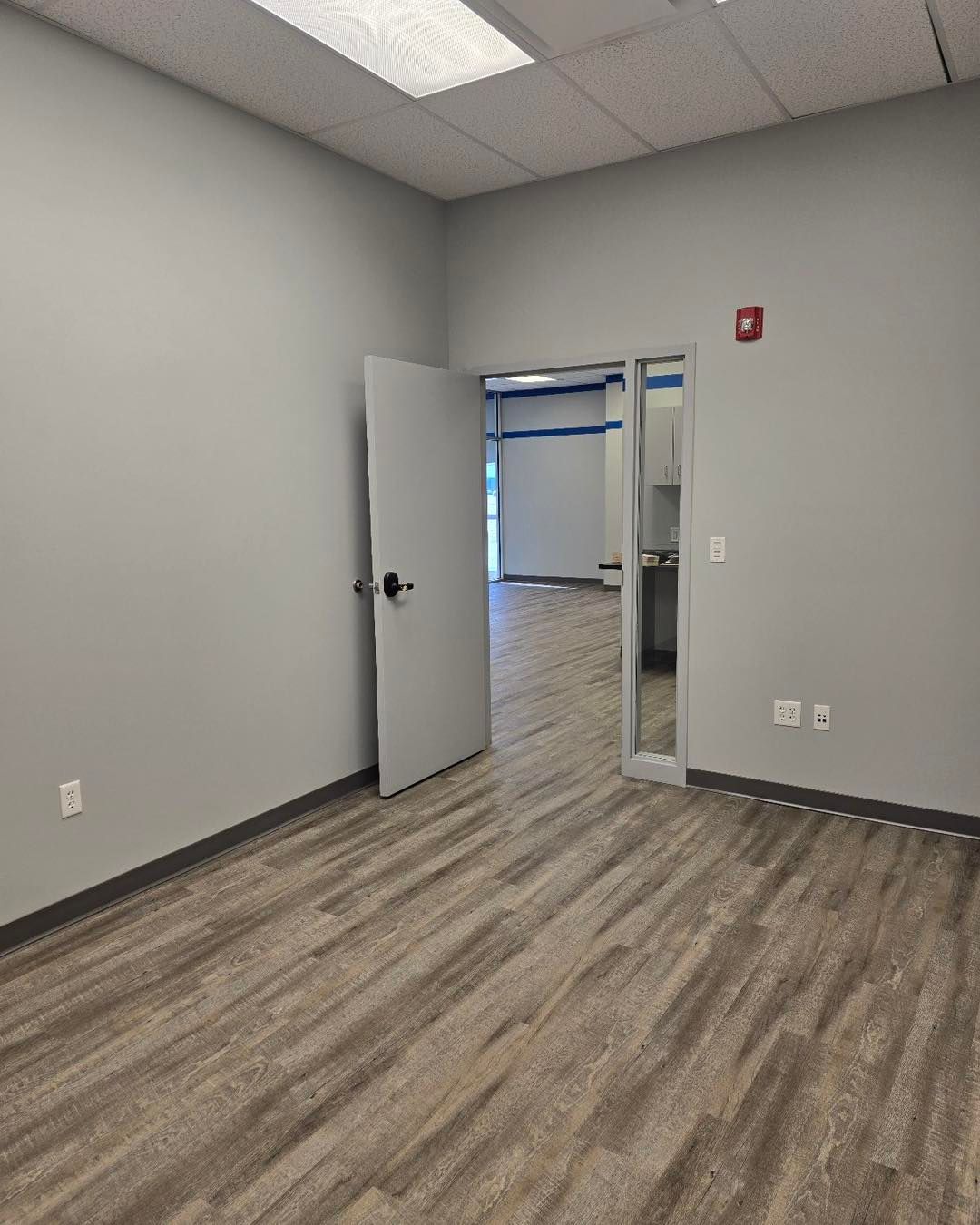 An empty room with hardwood floors and a door leading to a kitchen.