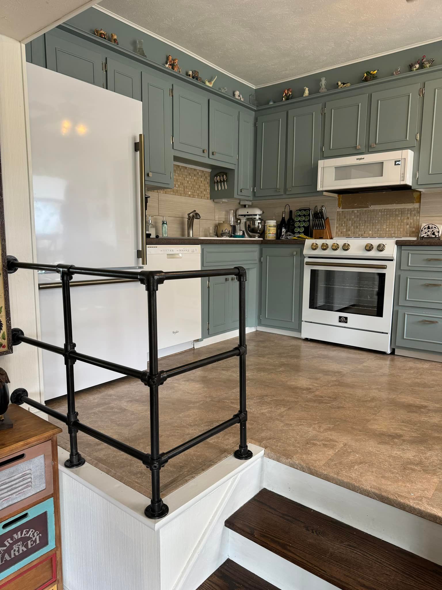 A kitchen with blue cabinets, white appliances, and a black railing.