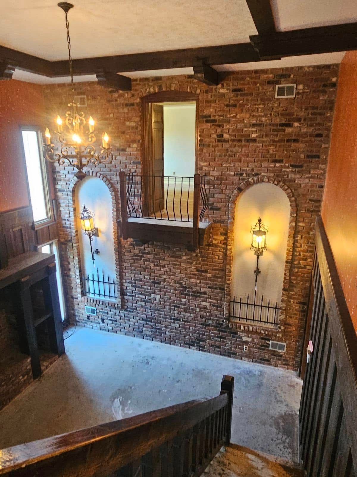 A staircase with a brick wall and a chandelier hanging from the ceiling.