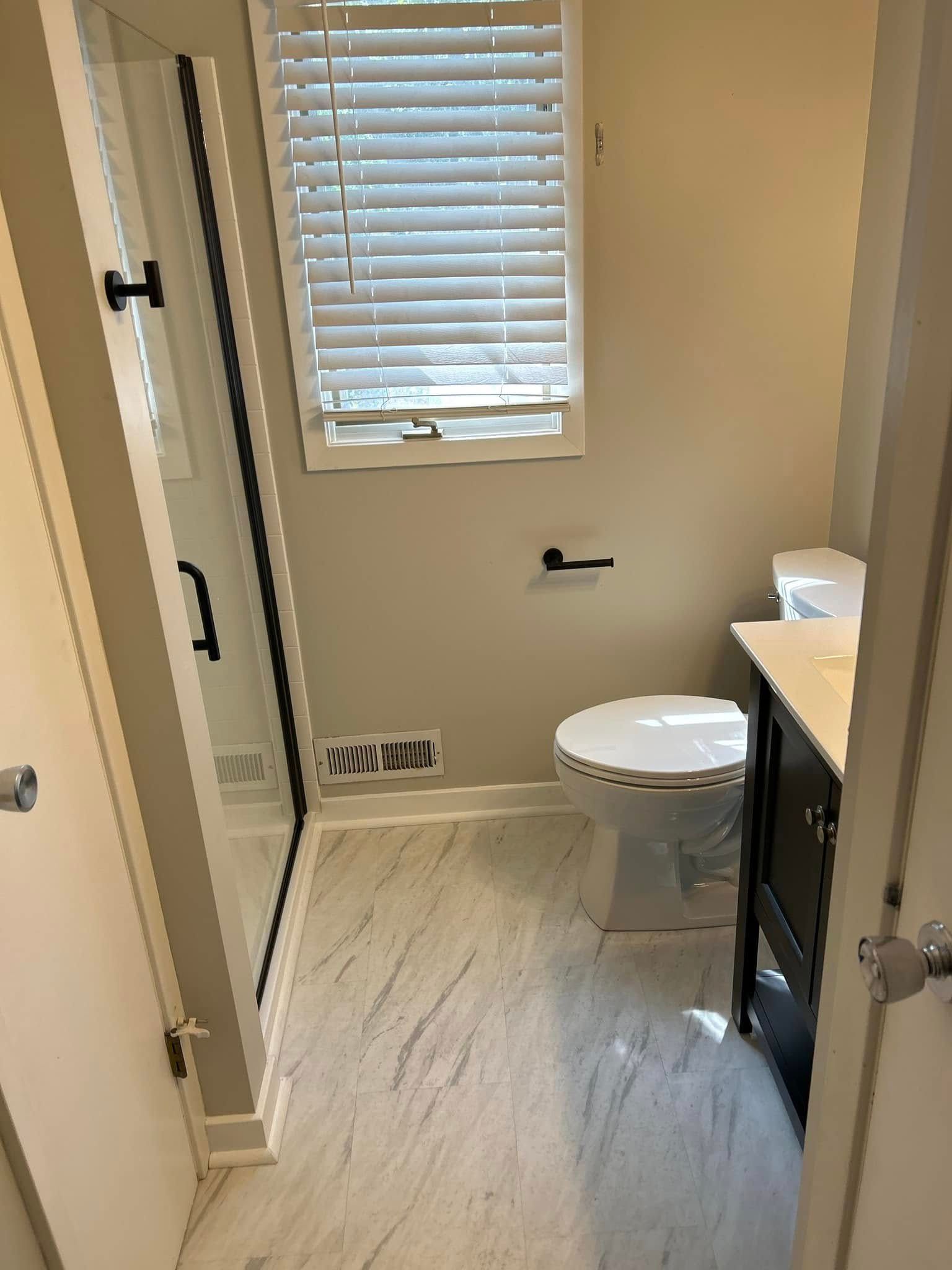 A bathroom with a toilet, sink, shower, and window.