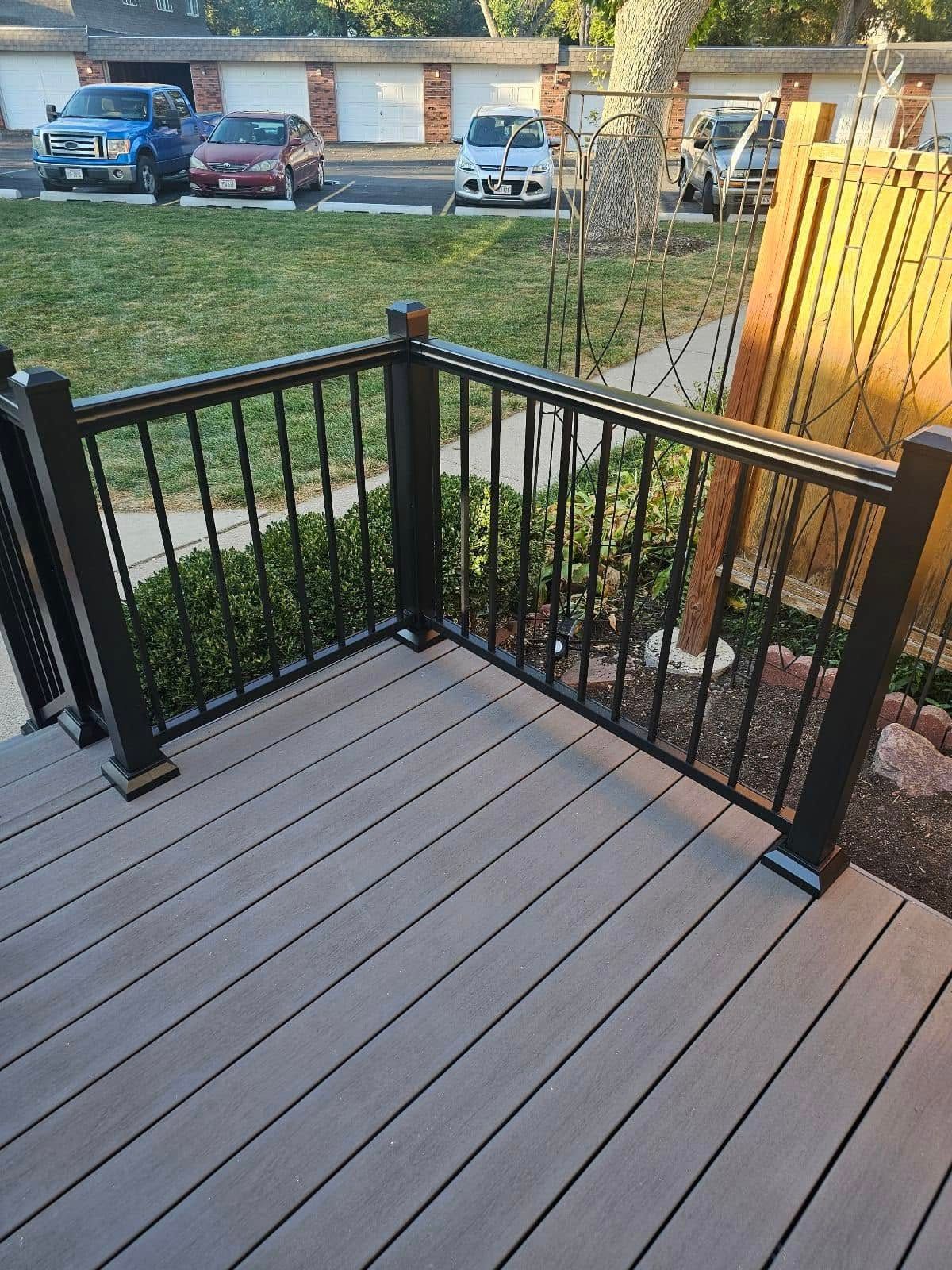A wooden deck with a black railing and cars parked in the background.