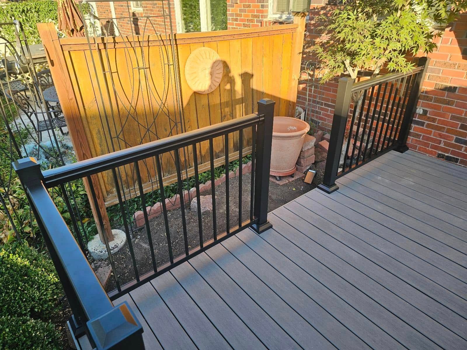 A wooden deck with a black railing and a fence in the background.
