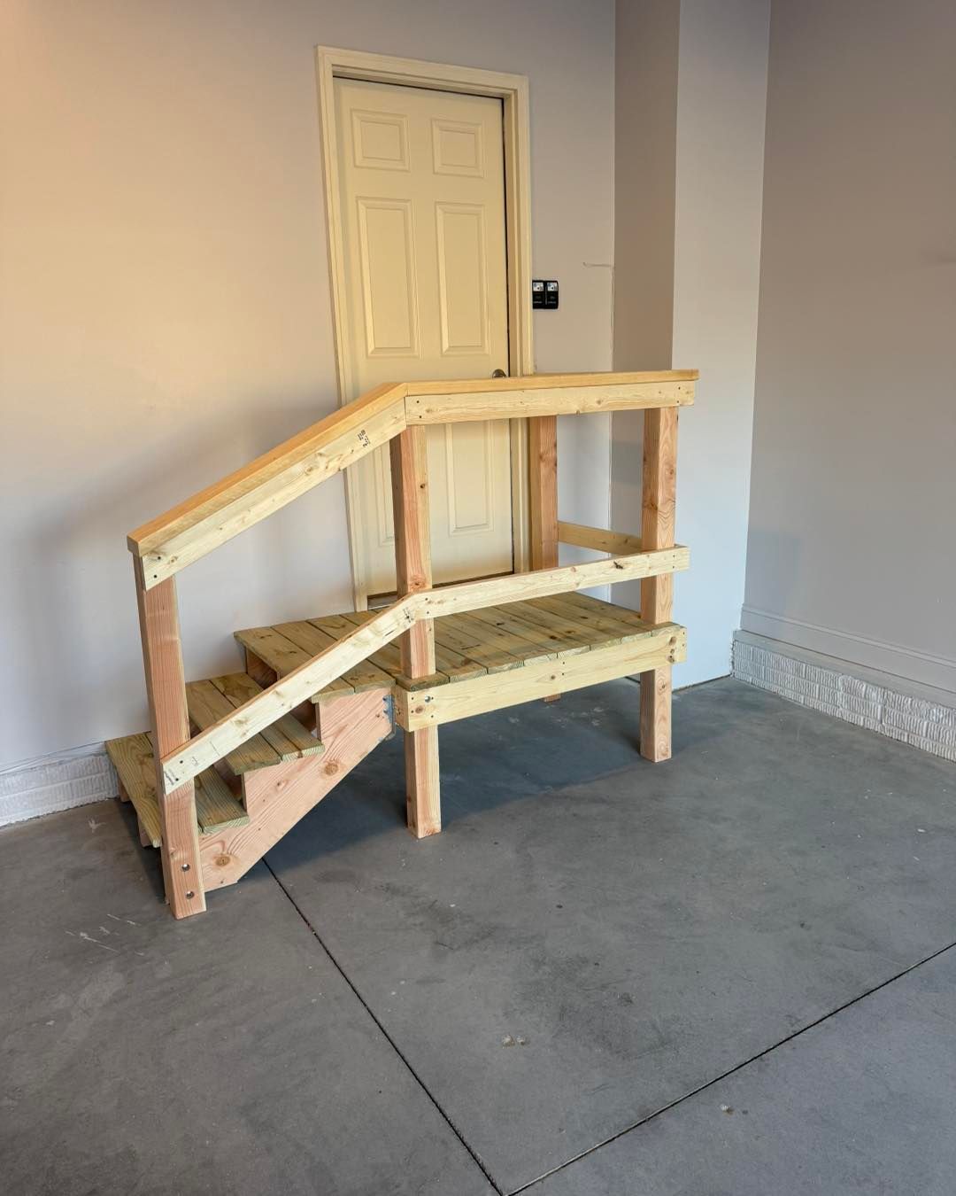 A wooden ramp with stairs in a garage next to a door.