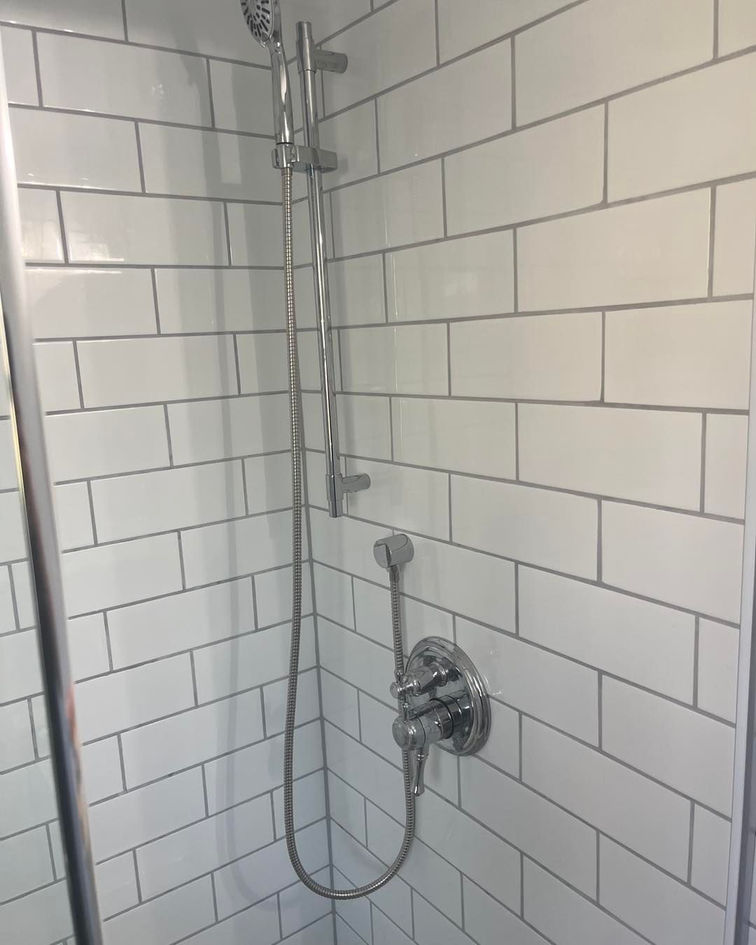 A shower with white tiles and a chrome shower head.